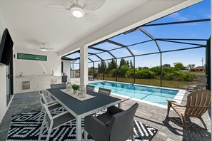 Ein moderner Poolbereich im Freien mit überdachter Terrasse, einem Esstisch mit Stühlen und Blick auf die umliegende Landschaft.