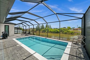 Ein überdachter Pool mit Seeblick, umgeben von einer Terrasse mit Stühlen und einem Grill.