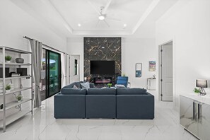Ein modernes Wohnzimmer mit Ecksofa, Flachbildfernseher, Kamin und Deckenventilator.