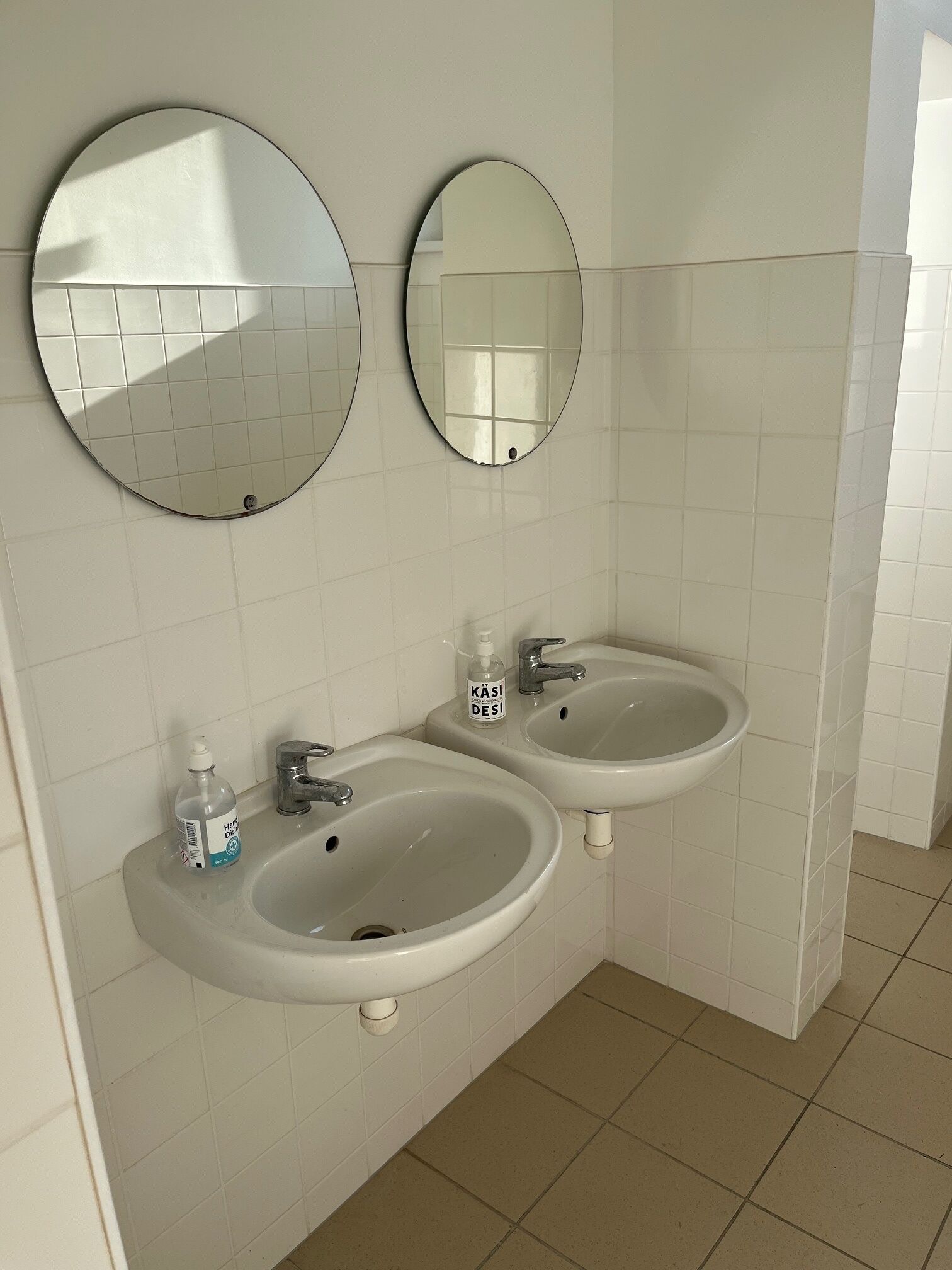 Een badkamer met twee wasbakken, een spiegel en een fles handdesinfectiemiddel.