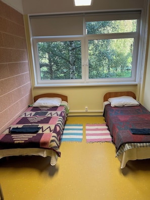 Une chambre avec deux lits, une fenêtre donnant sur des arbres et un mur en briques.