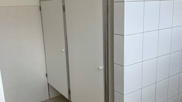 A restroom with white tiled walls and floor, a metal-framed stall door, and a hand dryer.