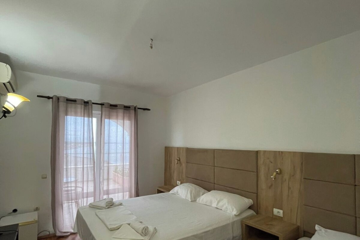 A hotel room with a large bed, a smaller bed, a desk, and a window with curtains.