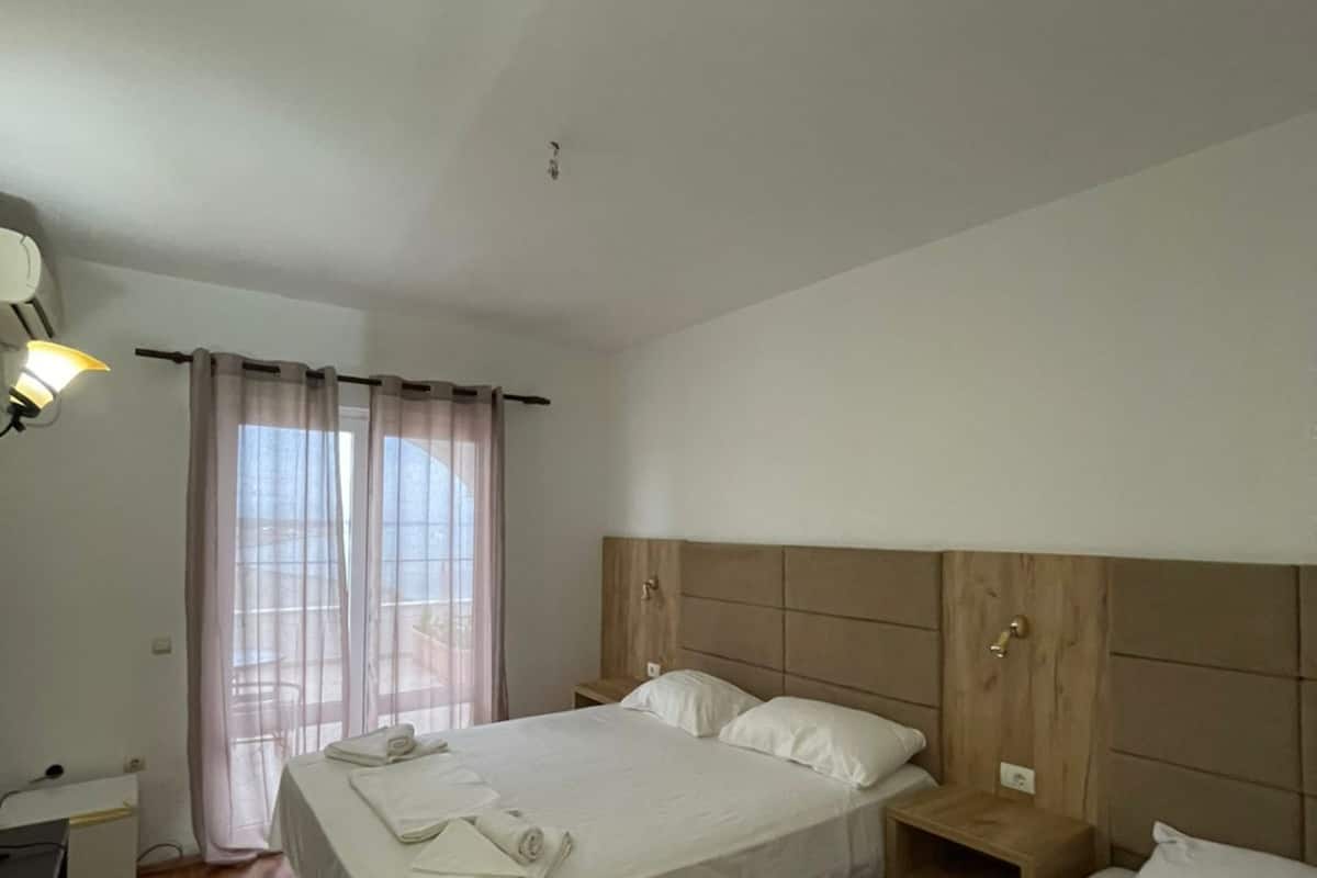 A hotel room with a large bed, a smaller bed, a desk, a chair, and a window with curtains.