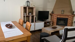Una sala de estar acogedora con una mesa de comedor de madera, sillas, un televisor, una estantería y una chimenea de ladrillo.