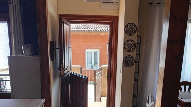 Un pasillo estrecho con piso de madera, una puerta que da a un espacio exterior y una lámpara en el techo.