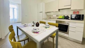 Una cocina moderna con armarios blancos, un microondas y un horno. Hay una mesa de comedor con sillas amarillas y un reloj en la pared.
