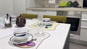 Una cocina con una mesa de comedor lista para cuatro personas, que incluye una cafetera, tetera, tazas y vasos.