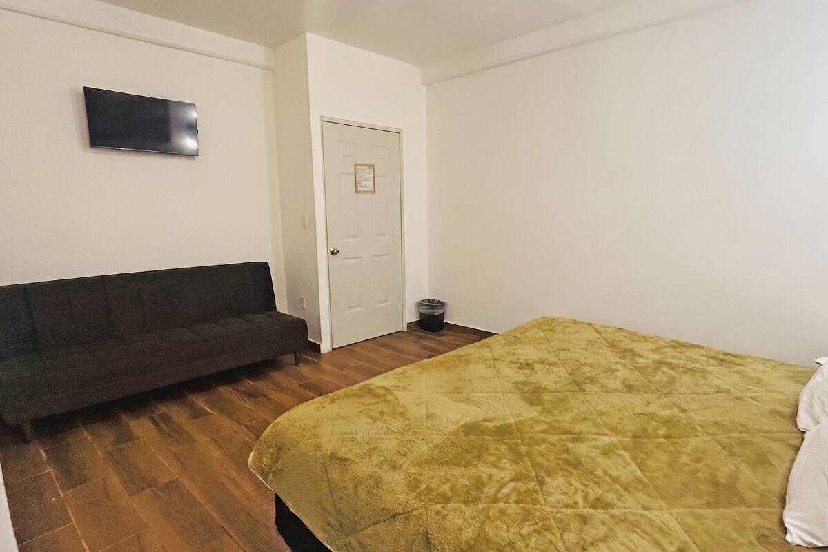 Una habitación con cama, sofá, puerta y televisor de pared.