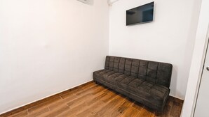 A room with a dark brown sofa, wooden flooring, a white wall, and a mounted flat-screen TV.