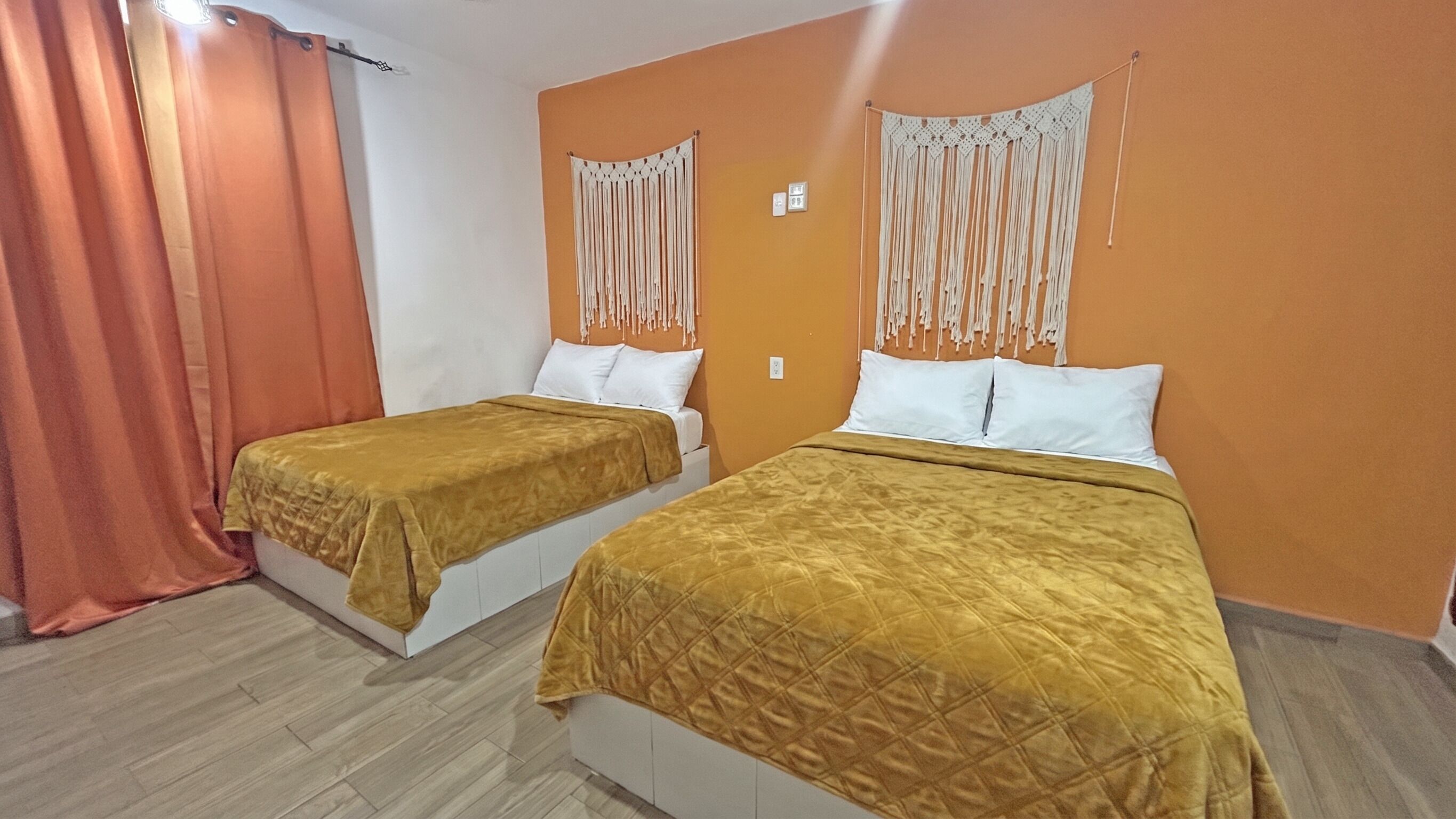 Ein Hotelzimmer mit zwei Betten, orangefarbenen Wänden und einem Vorhang.