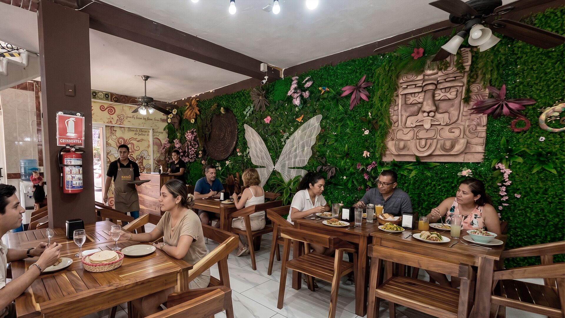 A restaurant with wooden tables and chairs, a green wall with decorative elements, and a ceiling fan.