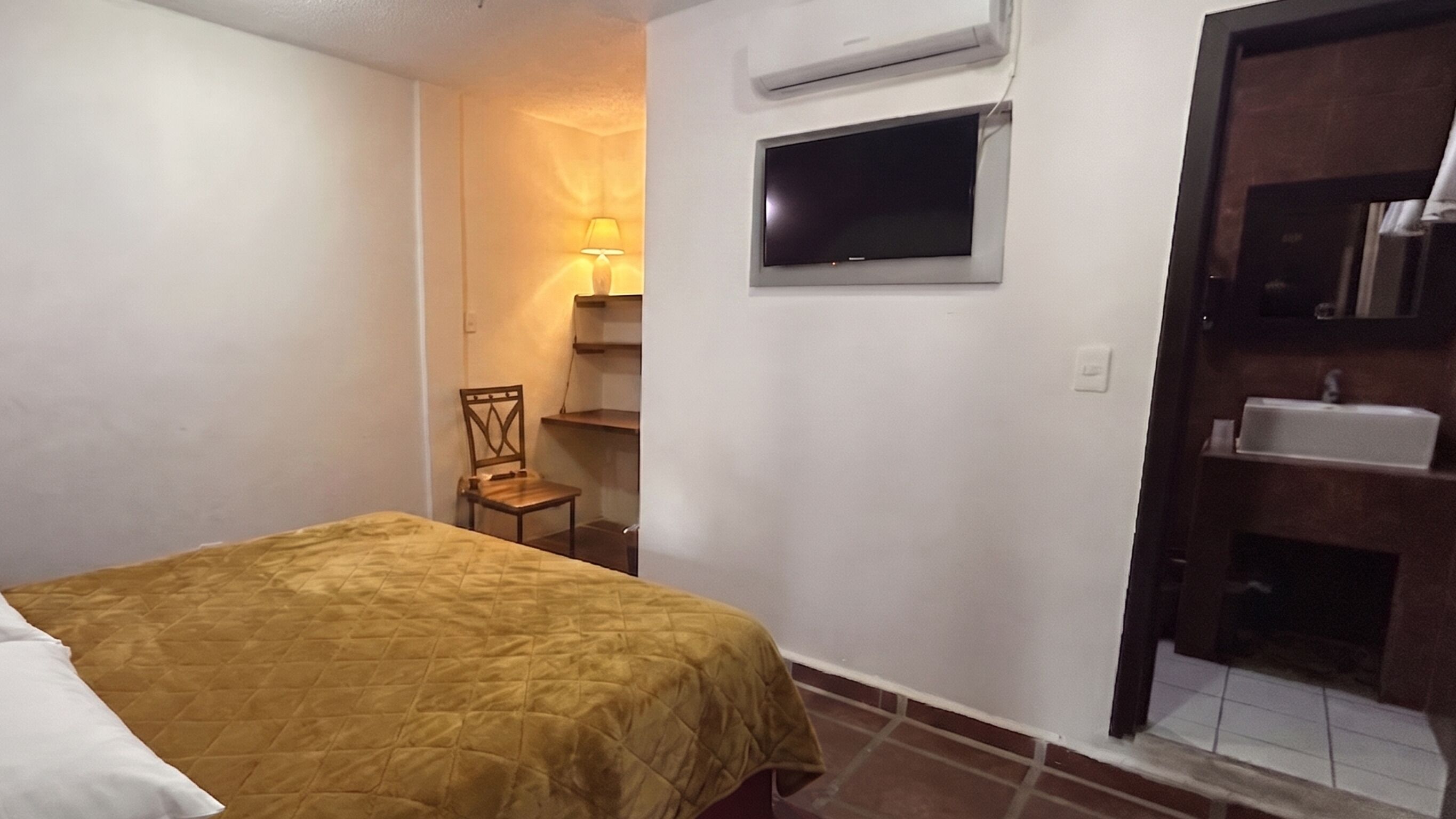 Ein Schlafzimmer mit Bett, Stuhl, Fernseher, Ablagefläche und Waschbecken.