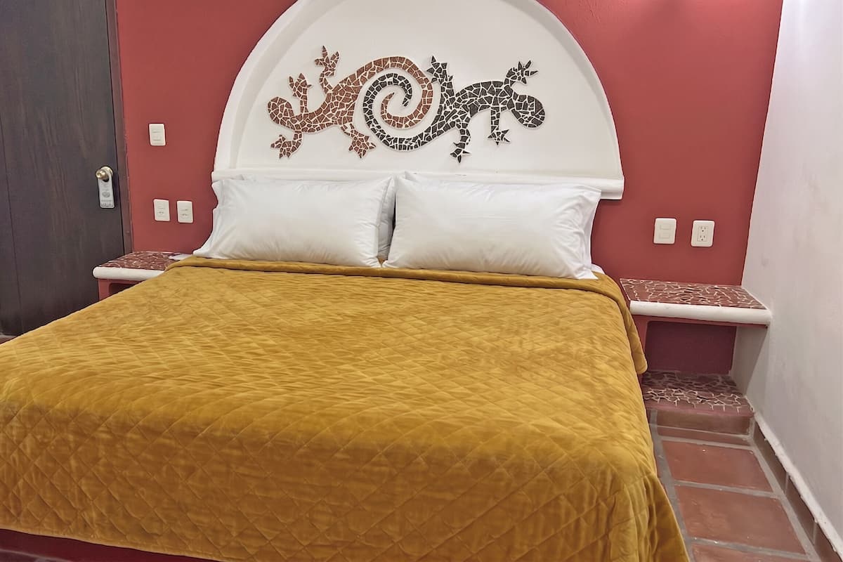 Una cama con cabecera acolchada, almohadas blancas y colcha color mostaza.