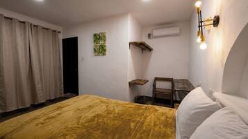 Une chambre à coucher comprenant un lit, un bureau, une chaise, un appareil de climatisation et un luminaire fixé au mur.