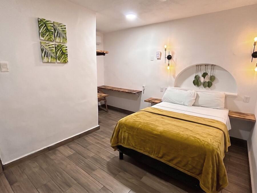 A bedroom with a bed, bedside tables, a desk, and wall-mounted lighting.