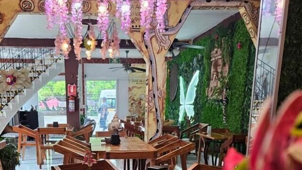 A restaurant with wooden tables and chairs, hanging floral decorations, and a green wall with a butterfly mural.