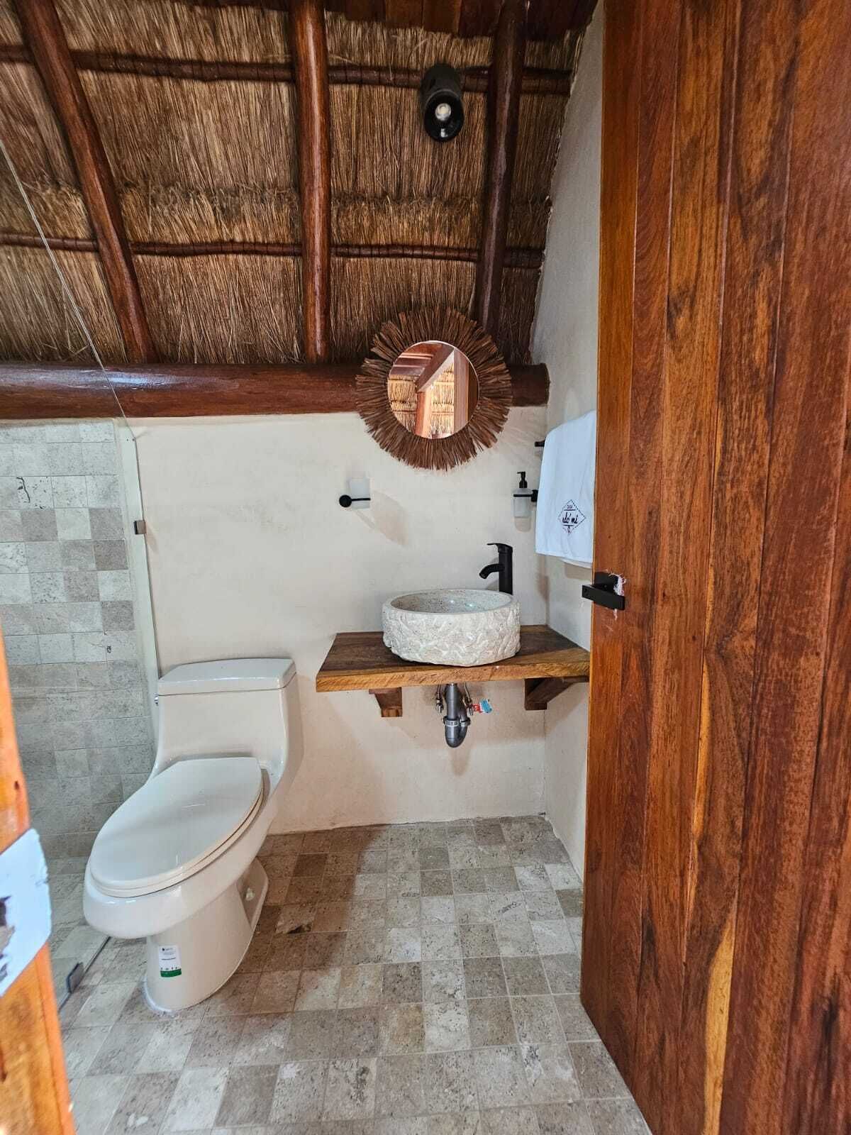 Ein Badezimmer mit rustikalem Holzboden, einem runden Spiegel, einer Toilette und einem Waschbecken mit Holzablage.