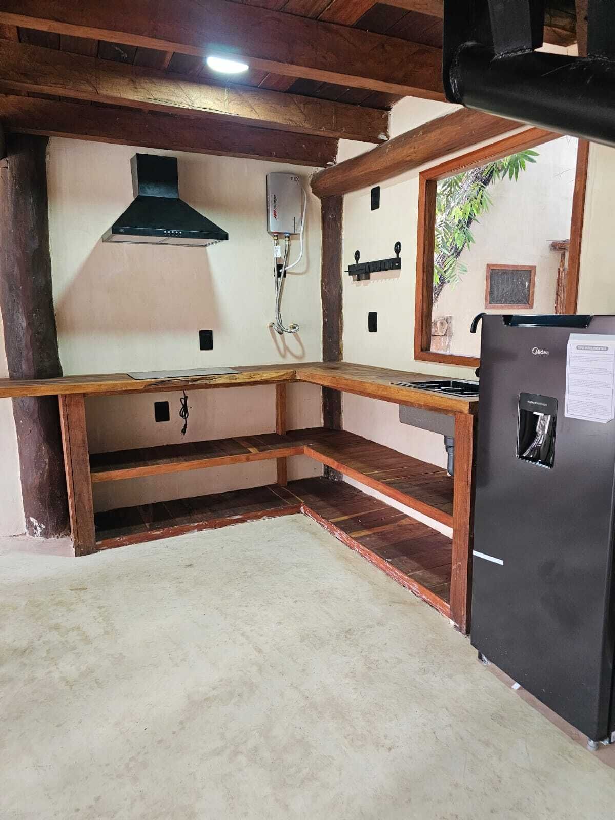 A kitchen with a wooden countertop, a black refrigerator, and a wall-mounted gas stove.