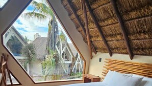 A bedroom with a bed, a wooden floor, a thatched roof, and a large window. - KAAJ NDOMI (Bacalar)