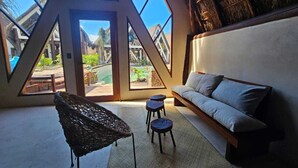 A room with a sloped ceiling, a sofa, a woven chair, and stools. - KAAJ NDOMI (Bacalar)