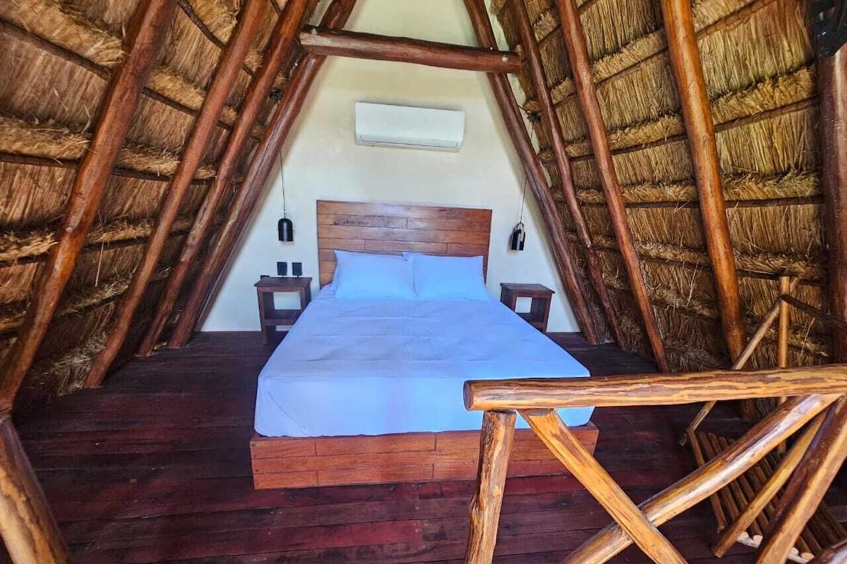 Una habitación con una cama de madera, techo de paja y piso de madera.