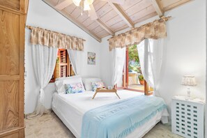 A bedroom with a bed, curtains, a bedside table, a lamp, and a window with a view. - 4-bedroom Villa in beautiful Savaneta with cool AC (Savaneta)