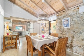 A dining area with a table set for four, wooden chairs, a stone wall, and a rustic ceiling. - 4-bedroom Villa in beautiful Savaneta with cool AC (Savaneta)