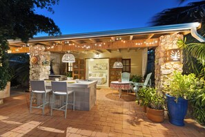 An outdoor patio area with a stone wall, a bar with bar stools, and potted plants. - 4-bedroom Villa in beautiful Savaneta with cool AC (Savaneta)