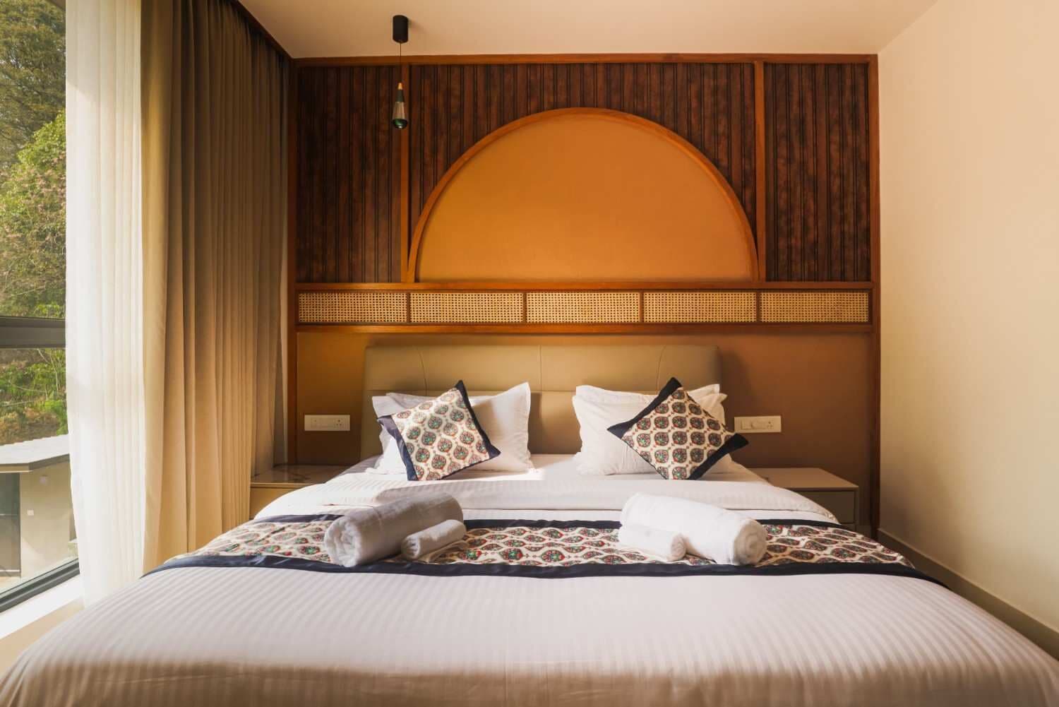 A hotel room with a bed, a large window, and a view of greenery outside.