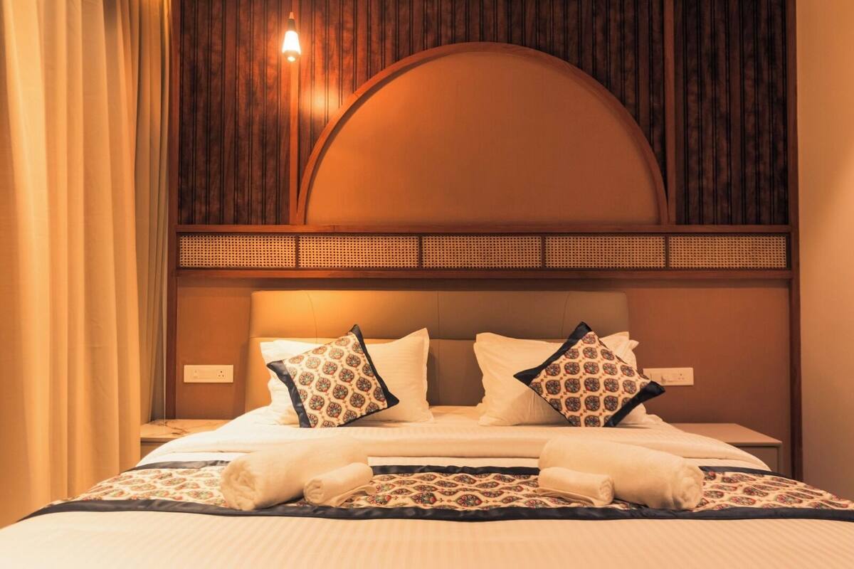 Una habitación de hotel con cama, almohadas, cabecera y mesita de noche.