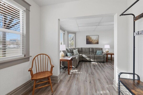 A living room with a sectional sofa, a wooden chair, a lamp, and a painting on the wall.