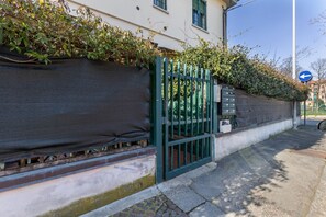 A gated entrance with a metal gate, a wall with a dark covering, and a blue directional sign. - Cozy 39m2 studio, ideal for an adult and a child up to 10 years old, located on the ground floor in lively Bolognina district. The location is strategic: the Fair, Tecnopolo & ring road are easily reachable, as are Central Station, the new Municipality h (Bologna)