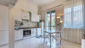 A modern kitchen with white cabinets, a dining table with chairs, and a large window with curtains. - Cozy 39m2 studio, ideal for an adult and a child up to 10 years old, located on the ground floor in lively Bolognina district. The location is strategic: the Fair, Tecnopolo & ring road are easily reachable, as are Central Station, the new Municipality h (Bologna)