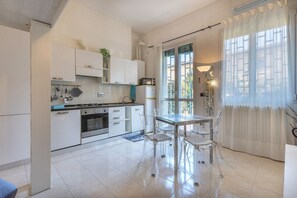 A modern kitchen with white cabinets, a dining table with chairs, and a large window with curtains. - Cozy 39m2 studio, ideal for an adult and a child up to 10 years old, located on the ground floor in lively Bolognina district. The location is strategic: the Fair, Tecnopolo & ring road are easily reachable, as are Central Station, the new Municipality h (Bologna)