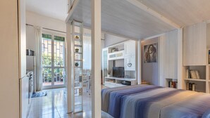 A modern bedroom with a bed, a TV, and a bookshelf. - Cozy 39m2 studio, ideal for an adult and a child up to 10 years old, located on the ground floor in lively Bolognina district. The location is strategic: the Fair, Tecnopolo & ring road are easily reachable, as are Central Station, the new Municipality h (Bologna)