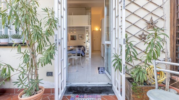 A doorway leading to a room with a bed, a chair, and a small table. There are potted plants on either side of the entrance. - Cozy 39m2 studio, ideal for an adult and a child up to 10 years old, located on the ground floor in lively Bolognina district. The location is strategic: the Fair, Tecnopolo & ring road are easily reachable, as are Central Station, the new Municipality h (Bologna)