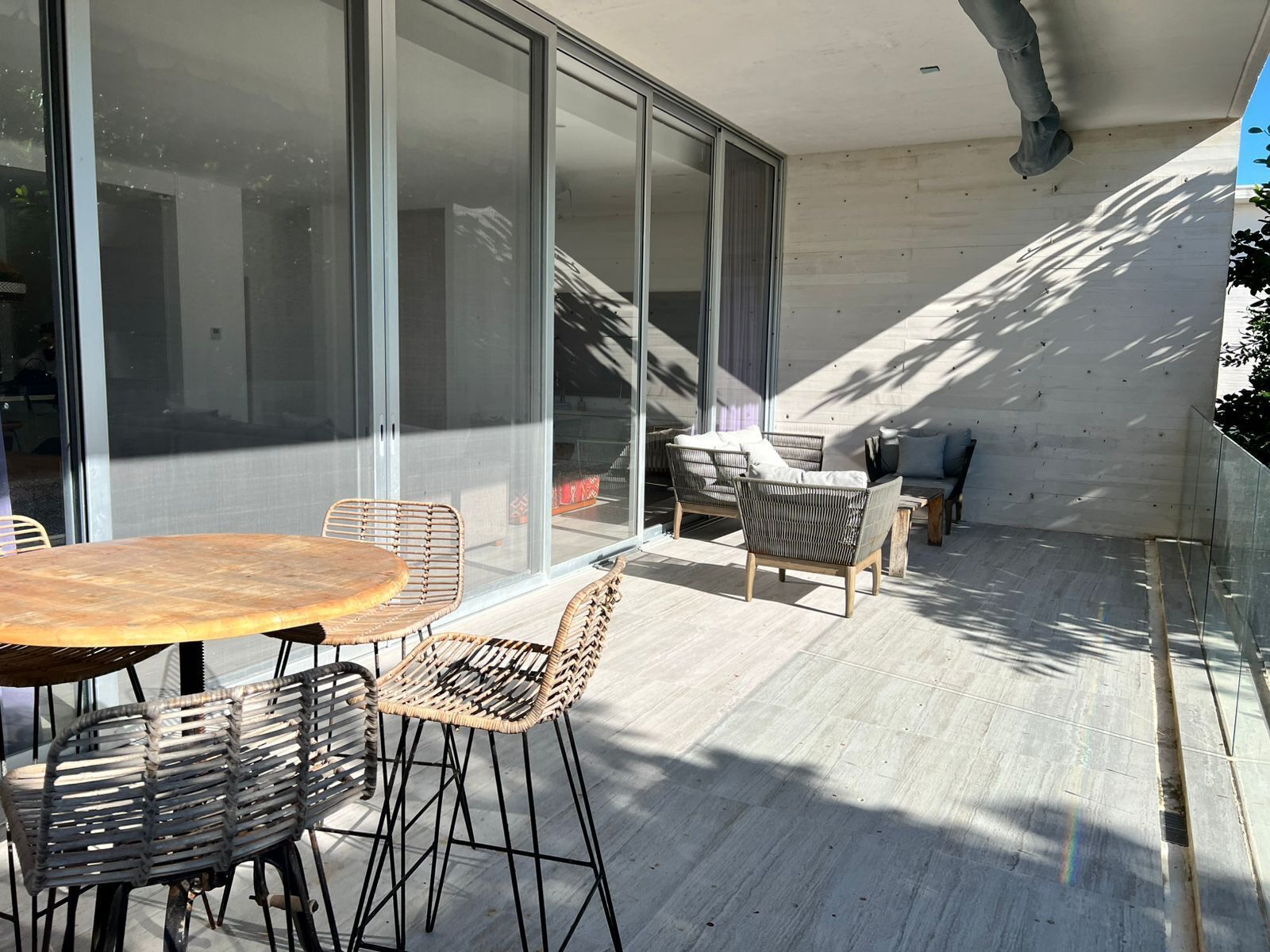 A modern outdoor seating area with a table and chairs, large sliding glass doors, and a view of the interior.