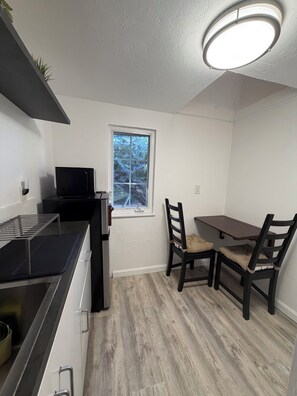 A compact kitchen with a microwave, a small window, and a dining area with two chairs and a table. - Private fenced guesthouse perfect for a couple, near Stanford, Google, Facebook (Palo Alto)