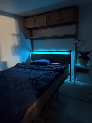 A bedroom with a bed, a nightstand, a potted plant, and a window with blue lighting. - Private fenced guesthouse perfect for a couple, near Stanford, Google, Facebook (Palo Alto)
