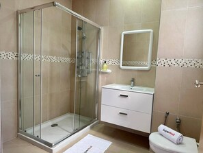 Un baño moderno con ducha de vidrio, un lavamanos blanco con espejo y un inodoro con una toalla que dice 'Superhost'.