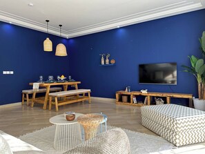 Ein modernes Wohnzimmer mit blauer Wand, Holzmöbeln, einem Fernseher und einem Essbereich.