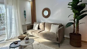 Ein modernes Wohnzimmer mit einem beige farbenen Sofa, einem runden Couchtisch, einer Topfpflanze und einem dekorativen Spiegel an der Wand.