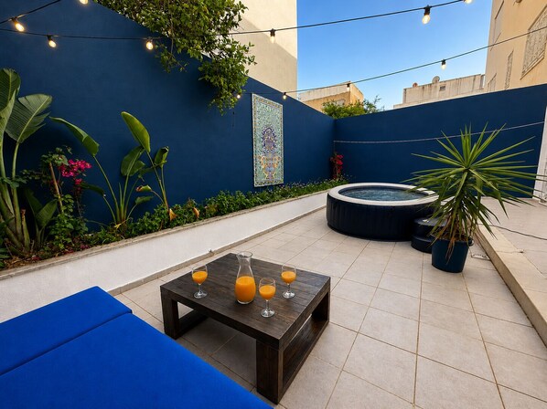 Un patio con una mesa dispuesta para cuatro personas, rodeado de plantas y un muro decorativo.