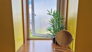 Une fenêtre donnant sur un jardin, une plante en pot et un miroir posé sur une étagère en bois.