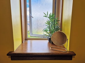 Una ventana con vistas a un jardín, una planta en maceta y un espejo sobre un repisa de madera.