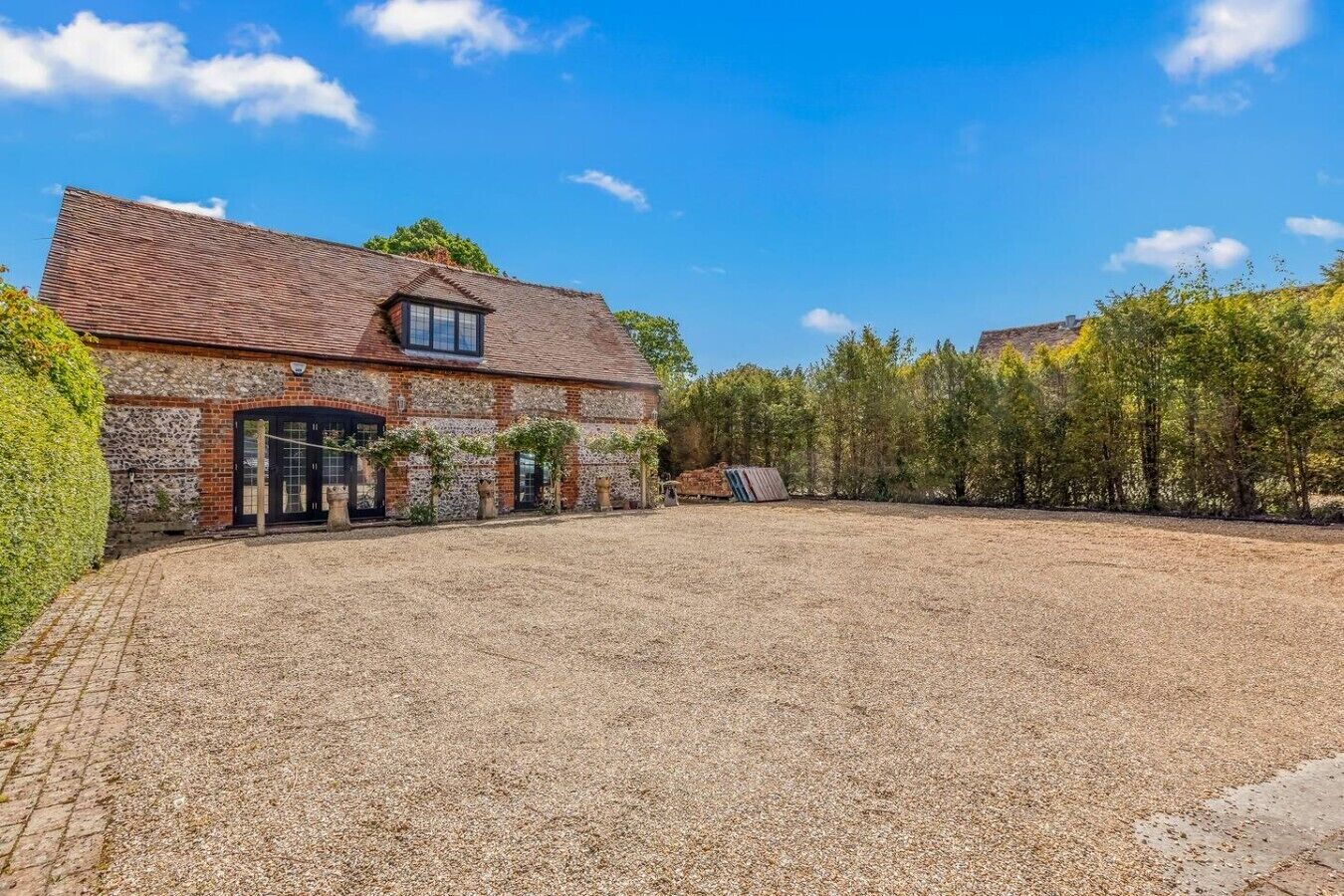 A rustic stone building with a tiled roof, a paved driveway, and a gravel courtyard.