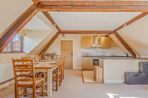 Eine Loft-Küche mit Holzbalken, ein Essbereich mit Tisch und Stühlen sowie ein Blick ins Freie.