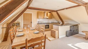 Zona pranzo con tavolo e sedie in legno, cucina con mobili in legno e camera soppalcata con travi a vista.