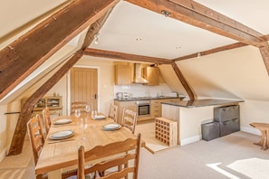 Ein Essbereich mit Holztisch und Stühlen, eine Küche mit Holzausbau und ein Schlafzimmer auf dem Dachboden mit freiliegenden Holzbalken.